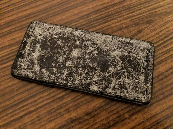 Téléphone portable avec verre cassé sur un fond en bois sombre. — Photo
