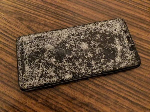 Téléphone portable avec verre cassé sur un fond en bois sombre. — Photo