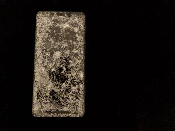 Telefone celular com vidro quebrado em um fundo preto . — Fotografia de Stock