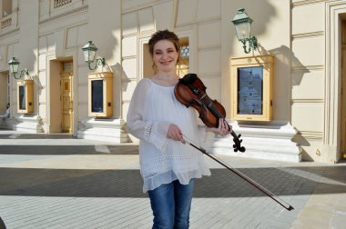 Beyaz bluzlu hamile bir kız. Sarışın kız. Genç bir kız. Keman çalan kız.