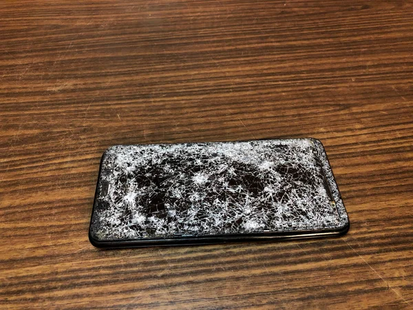 Ponsel dengan kaca pecah pada latar belakang kayu gelap. — Stok Foto