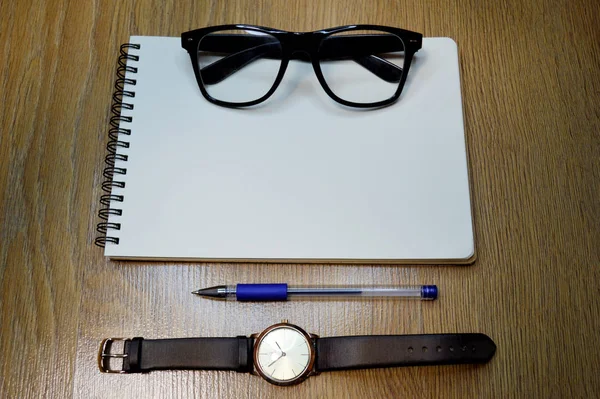 Reloj de muñeca, cuaderno, bolígrafo y gafas sobre fondo de madera —  Fotos de Stock