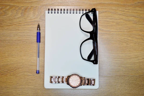Armbandsur, anteckningsbok, penna och glasögon på trä bakgrund — Stockfoto