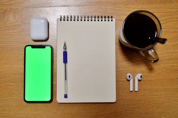 Telefon, słuchawki bezprzewodowe, notebook, kawa i długopis na drewnianym tle — Zdjęcie stockowe