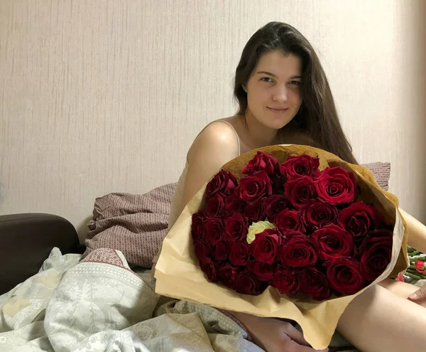 Bella ragazza seduta a letto con un enorme mazzo di rose . — Foto Stock