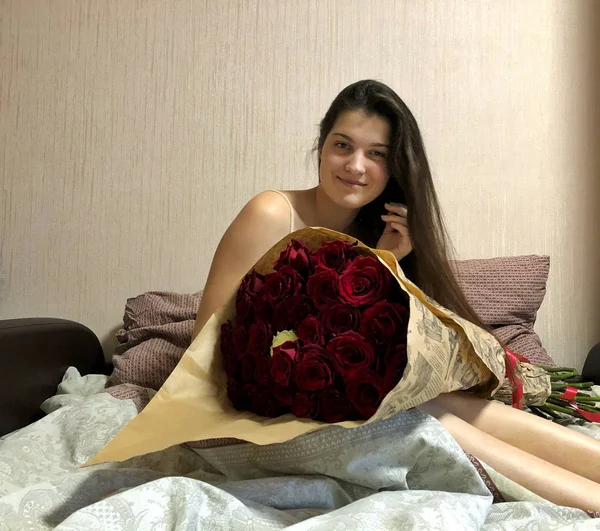 Bella ragazza seduta a letto con un enorme mazzo di rose . — Foto Stock