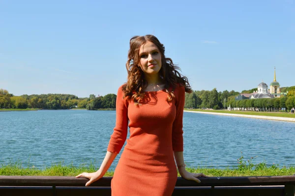 Young girl in orange dress stands near the water. — 스톡 사진