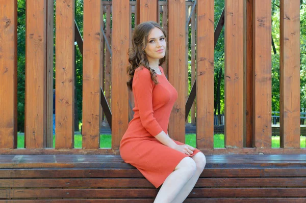 Ung flicka i orange klänning sitter på en bakgrund av träbjälkar. — Stockfoto