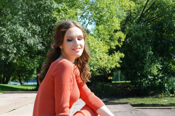 Junges Mädchen in orangefarbenem Kleid sitzt auf einem Steg am Wasser. — Stockfoto