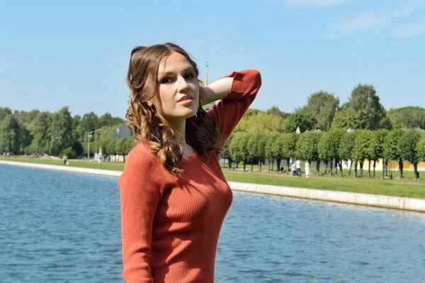 Young girl in orange dress stands near the water. — 스톡 사진