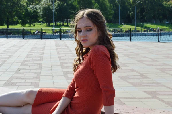 Menina jovem em vestido laranja senta-se em um fundo de vigas de madeira . — Fotografia de Stock