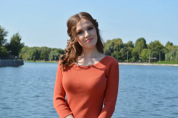 Menina jovem em vestido laranja fica perto da água . — Fotografia de Stock