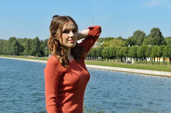 Menina jovem em vestido laranja fica perto da água . — Fotografia de Stock