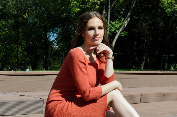 オレンジのドレスの若い女の子は水の近くの桟橋に座っている. — ストック写真