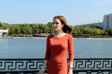 Turuncu elbiseli genç kız suyun yanında duruyor..