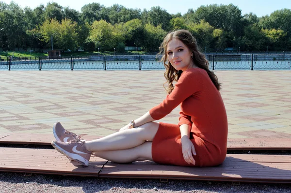 Chica joven en vestido naranja se sienta sobre un fondo de vigas de madera . — Foto de Stock