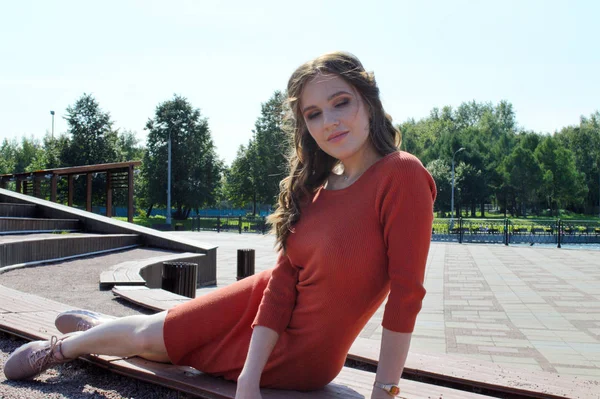 Menina jovem em vestido laranja senta-se em um fundo de vigas de madeira . — Fotografia de Stock