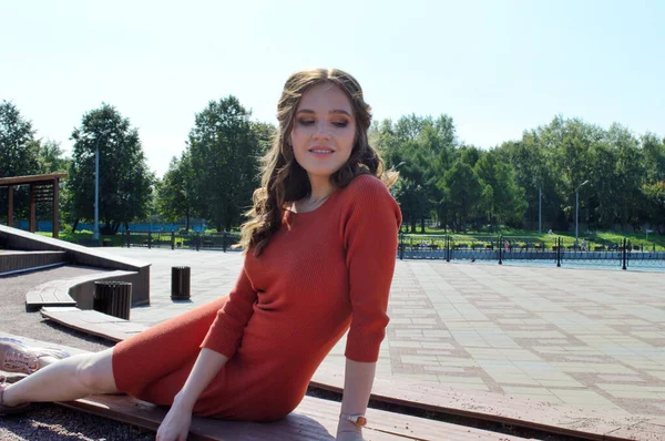 Chica joven en vestido naranja se sienta sobre un fondo de vigas de madera . —  Fotos de Stock