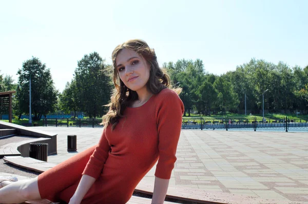 Menina jovem em vestido laranja senta-se em um fundo de vigas de madeira . — Fotografia de Stock