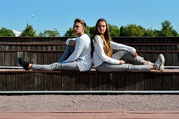Молодая девушка и молодой человек в одной одежде сидят на деревянной скамейке . — стоковое фото