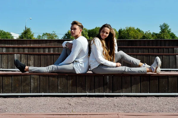 Een jong meisje en een jonge man in dezelfde kleren zittend op een houten bank. — Stockfoto