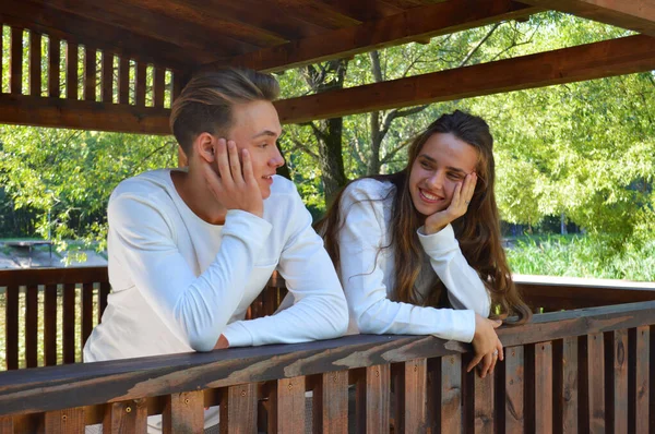 En ung flicka och en ung man i samma kläder sitter på en träbänk. — Stockfoto