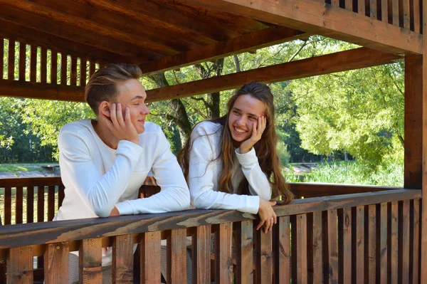 Молодая девушка и молодой человек в одной одежде сидят на деревянной скамейке . — стоковое фото