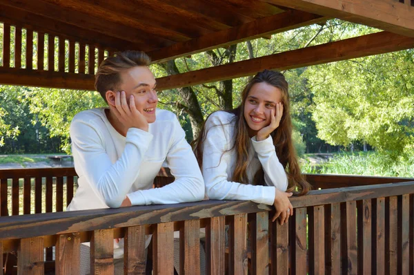 Una giovane ragazza e un giovane con gli stessi vestiti seduti su una panchina di legno . — Foto Stock