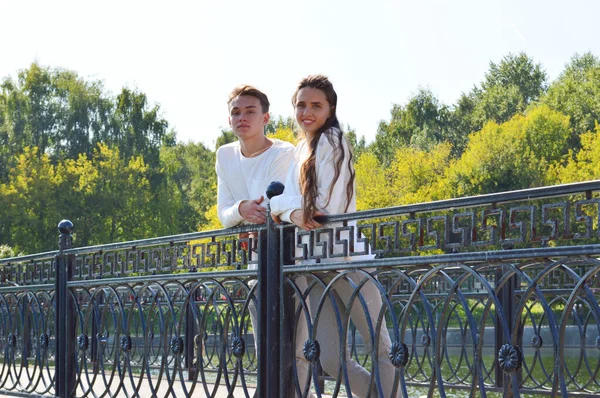 En ung flicka och en ung man i samma kläder på en bro nära vattnet. — Stockfoto
