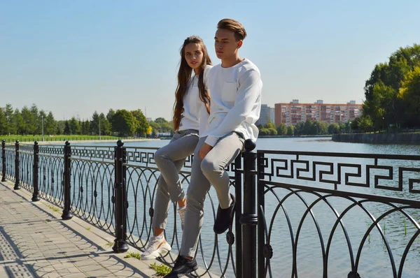 Uma jovem e um jovem com as mesmas roupas em uma ponte perto da água . — Fotografia de Stock