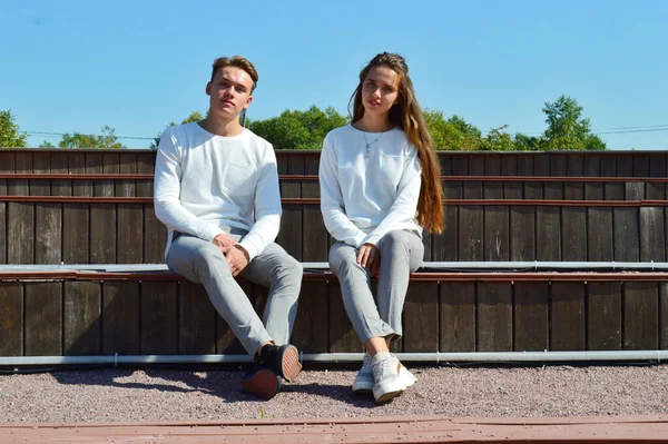 A young girl and a young man in the same clothes sitting on a wooden bench. — Stock Photo, Image