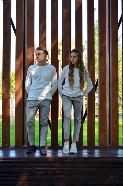 En ung flicka och en ung man i samma kläder på en träbänk. — Stockfoto