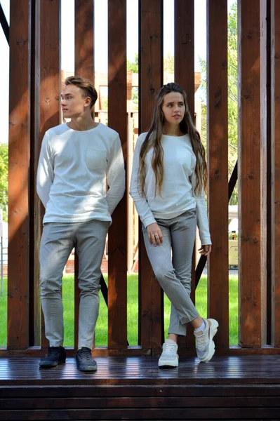 A young girl and a young man in the same clothes on a wooden bench. — Stock Photo, Image