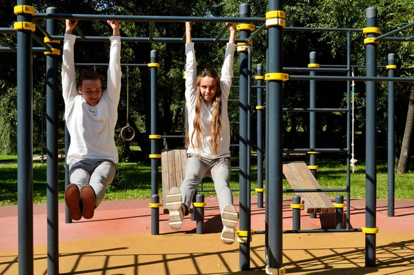 Ein junges Mädchen und ein junger Mann in derselben Kleidung auf dem Spielplatz. — Stockfoto