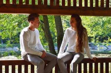 Genç bir kız ve aynı kıyafetleri giyen genç bir adam ahşap bir bankta oturuyor..