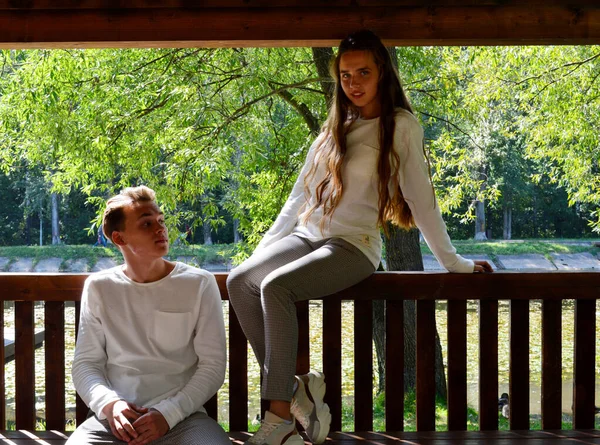 같은 옷을 입은 젊은 소녀와 나무 의자에 앉아 있는 젊은 남자. — 스톡 사진