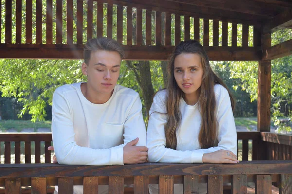 Ένα νεαρό κορίτσι και ένας νεαρός άνδρας με τα ίδια ρούχα κάθονται σε ένα ξύλινο παγκάκι. — Φωτογραφία Αρχείου