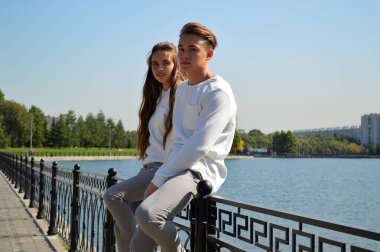 Suya yakın bir köprüde genç bir kız ve aynı kıyafetleri giyen genç bir adam.