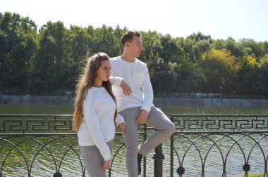 Suya yakın bir köprüde genç bir kız ve aynı kıyafetleri giyen genç bir adam.