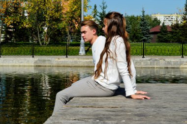 Genç bir kız ve aynı kıyafetleri giyen genç bir adam su kenarındaki ahşap bir iskelede