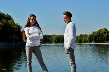 Genç bir kız ve aynı kıyafetleri giyen genç bir adam su kenarındaki ahşap bir iskelede