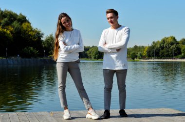 Genç bir kız ve aynı kıyafetleri giyen genç bir adam su kenarındaki ahşap bir iskelede