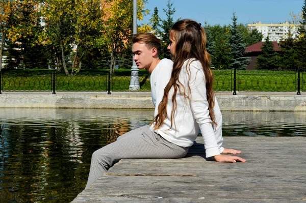 Genç bir kız ve aynı kıyafetleri giyen genç bir adam su kenarındaki ahşap bir iskelede