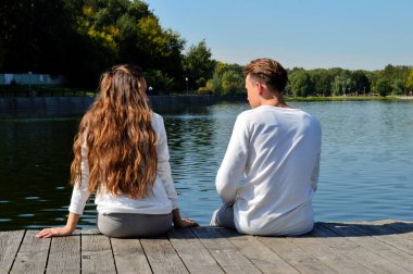 Genç bir kız ve aynı kıyafetleri giyen genç bir adam su kenarındaki ahşap bir iskelede