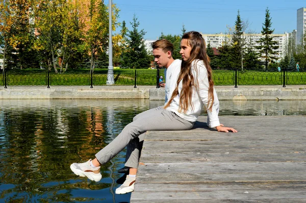 Genç bir kız ve aynı kıyafetleri giyen genç bir adam su kenarındaki ahşap bir iskelede