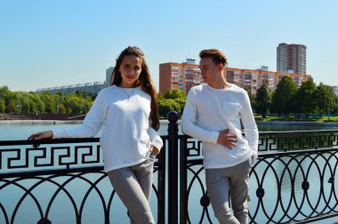 Suya yakın bir köprüde genç bir kız ve aynı kıyafetleri giyen genç bir adam.