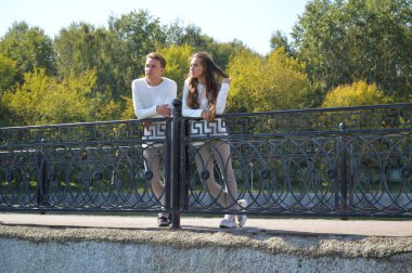 Suya yakın bir köprüde genç bir kız ve aynı kıyafetleri giyen genç bir adam.