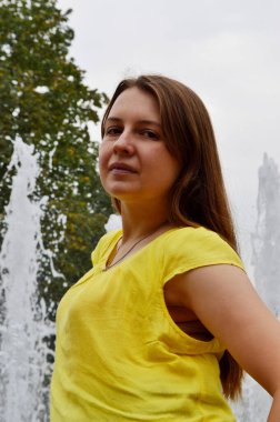 Çeşmenin yanında sarı tişörtlü, siyah saçlı kadın.