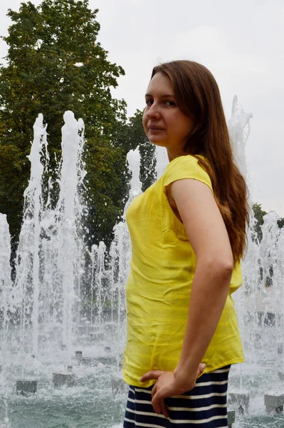 Woman with dark hair in a yellow T-shirt near the fountain