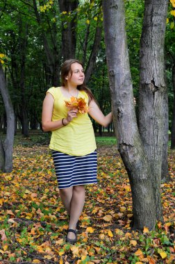 Sarı tişörtlü, siyah saçlı, sarı yapraklı bir kadın.